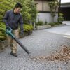 砂利を飛ばさないよう低い風量で落ち葉を掃除する日本人男性